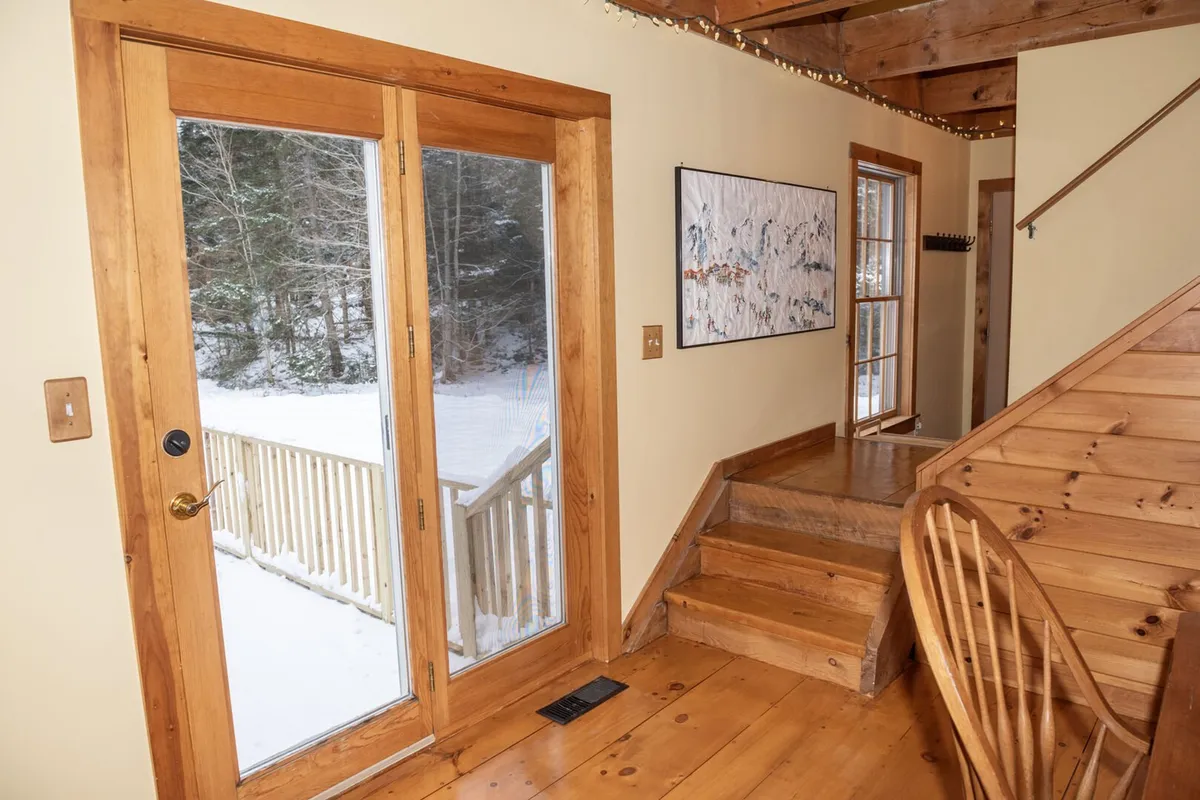 This image captures the home's double doors leading outside, a welcoming wooden staircase, and an art piece on the wall. The space gives the sense of entry and transition, likely functioning as or near a mudroom where guests prepare for or return from outdoor adventures. The scene feels cozy and ready for activity, embodying the idea of a launchpad for seasonal fun.