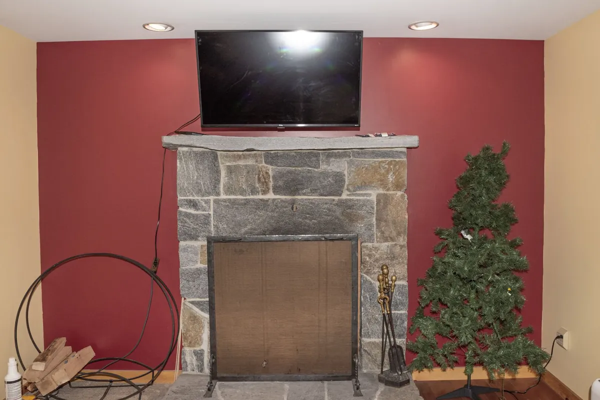 The scene centers on a stone fireplace, a television, and festive elements like a Christmas tree and decorative statues. The inviting living area features comfortable seating, creating a warm, welcoming atmosphere that encourages cozying up with pets after a day spent outside.