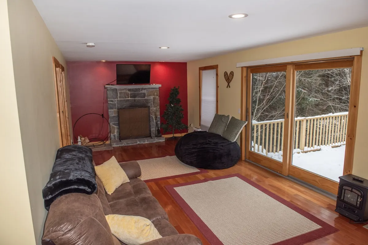 A cozy living space with a fireplace, large windows offering a view of the snowy outdoors, a comfortable sofa, and a bean bag chair—creating a perfect spot for gathering, relaxing, or watching TV.