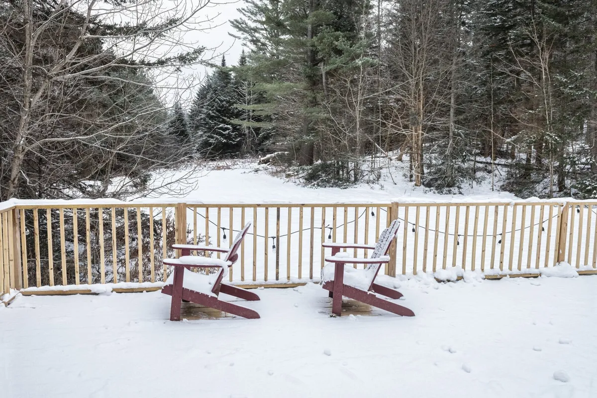 An exterior view of the chalet’s wooden deck, featuring red chairs, surrounded by snow and trees. This tranquil setting invites guests to step outside, relax, and enjoy the seamless connection to nature mentioned in the section.