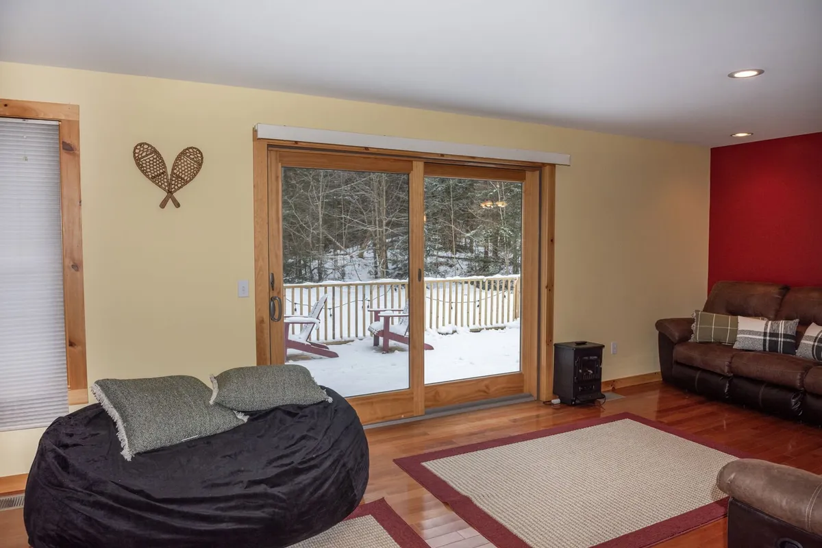 This image features a large sliding glass door that offers a connection between the cozy interior living space and the outdoors. It shows a bean bag chair and reclining sofa with decorative wall art, suggesting a spot where guests and their pets might relax after outdoor adventures. The ample natural light streaming in through the door hints at the surrounding natural landscape just beyond the glass.