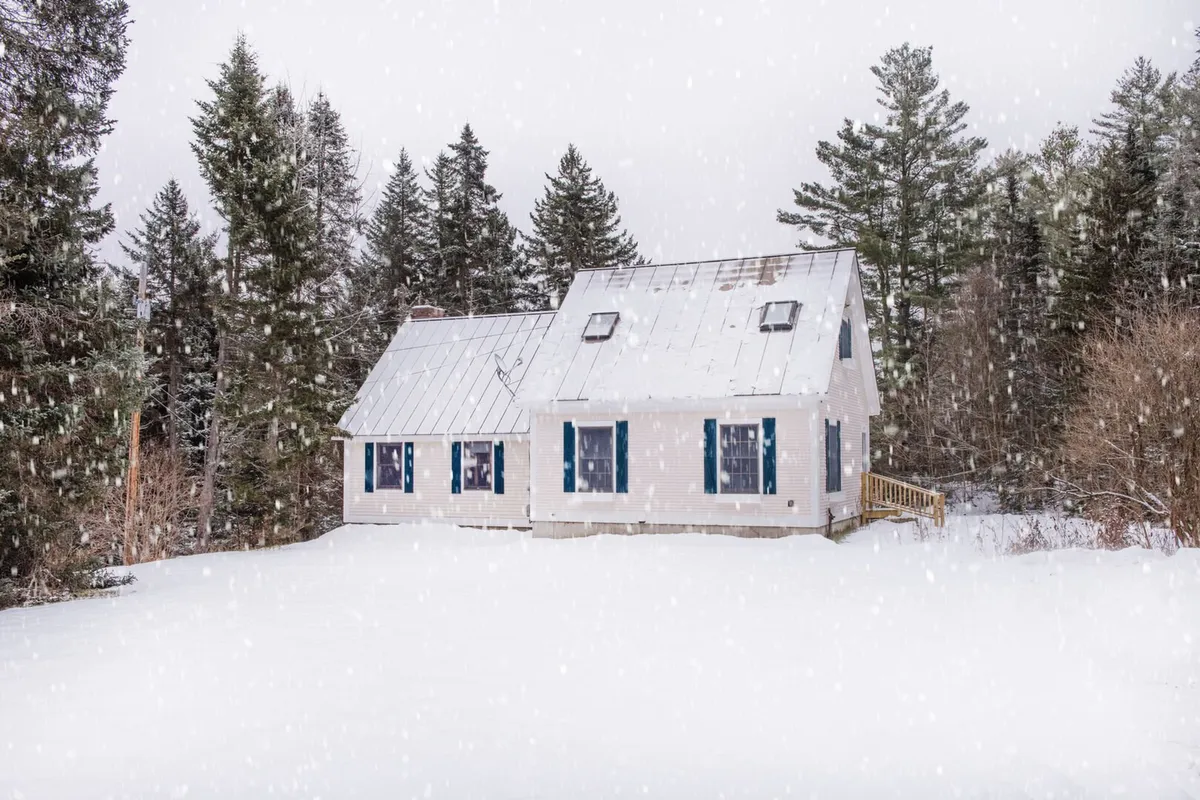 The hero image features a charming chalet nestled among snow-covered trees, its warm lights glowing from the windows. The expansive yard is blanketed in fresh snow, with ample open space perfect for winter play or peaceful moments enjoying the forested surroundings.