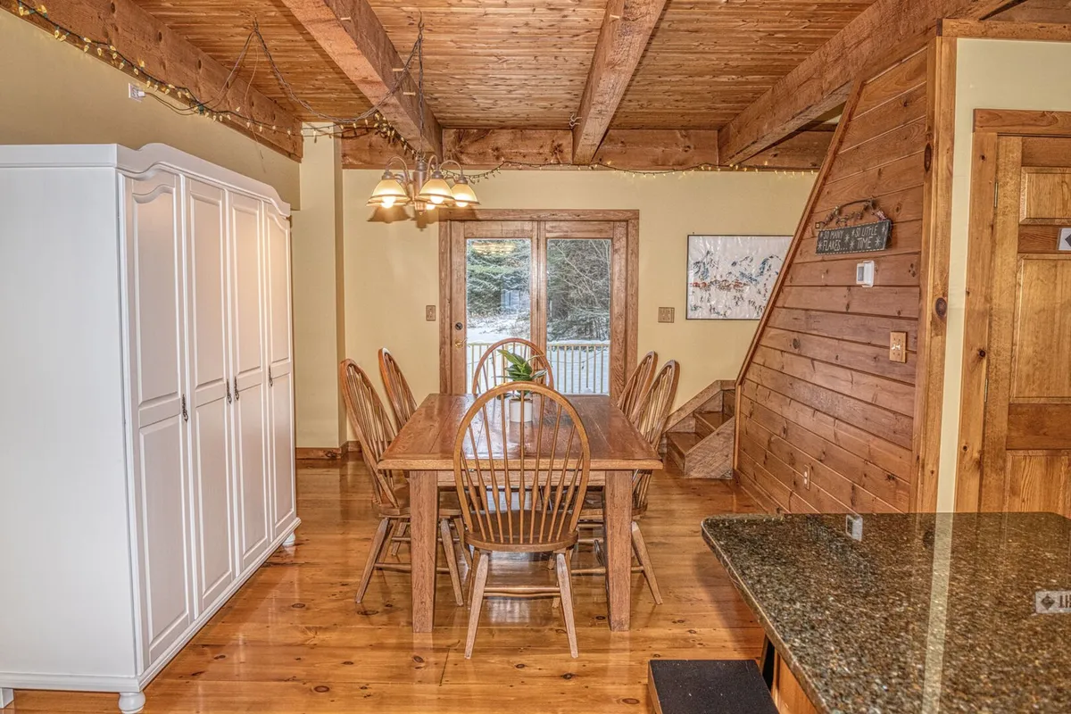 A welcoming dining space with a rustic wooden table, prominent ceiling beams, sliding glass doors opening to the outdoors, and cabinetry. The openness and view to the outside suggest easy access for picnics or returning from a day out, while the table itself invites communal activities.